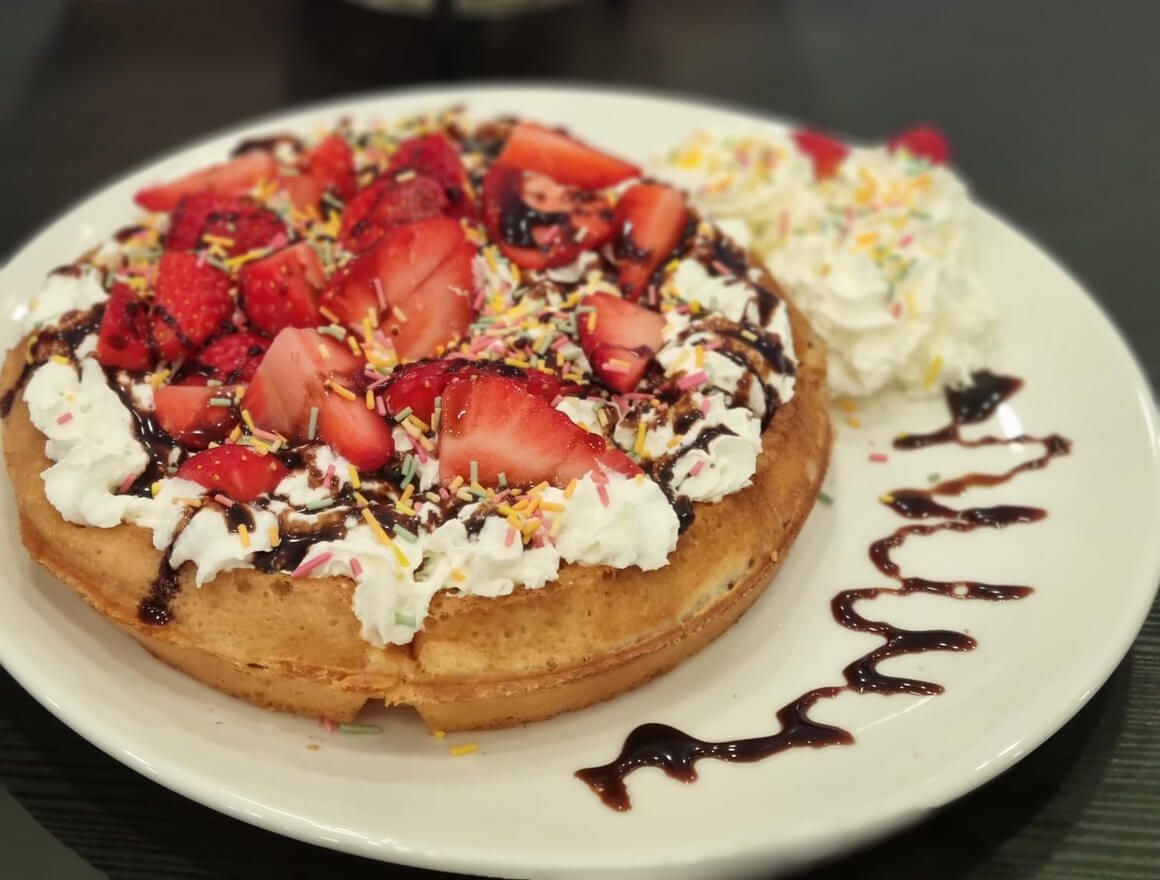 a waffle with strawberries and whipped cream on a white plate .