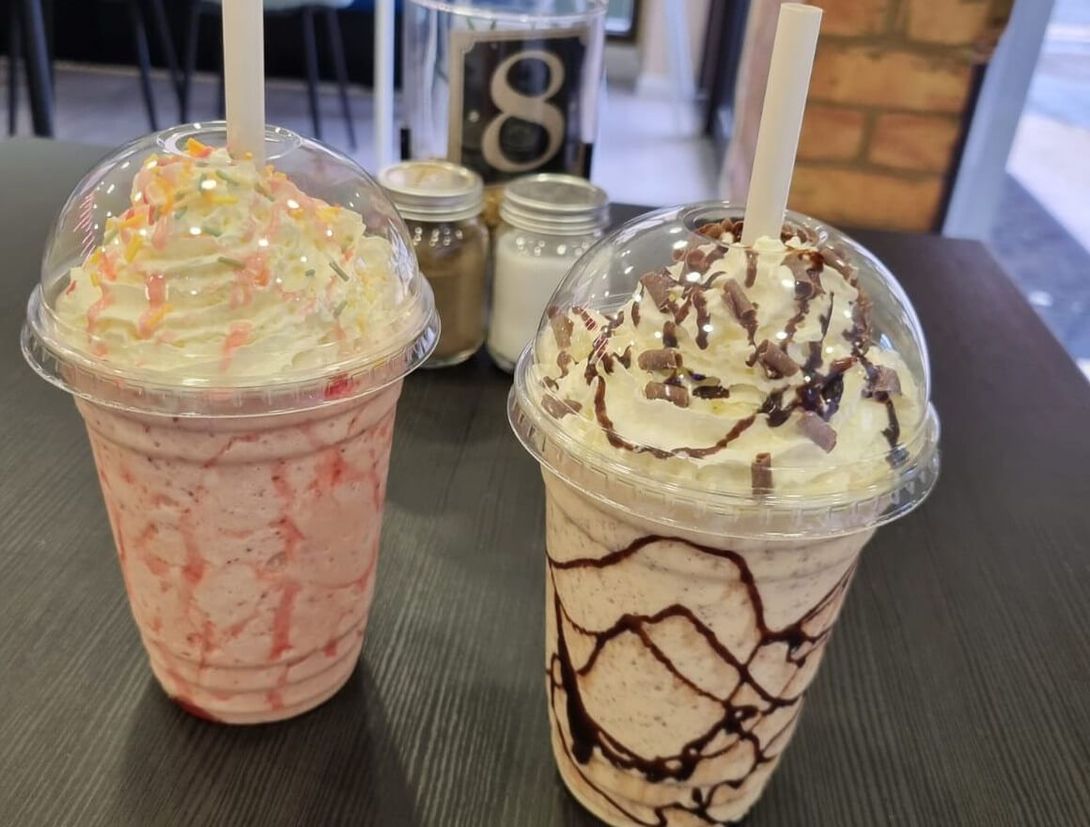 two milkshakes are sitting on a table with straws in them .