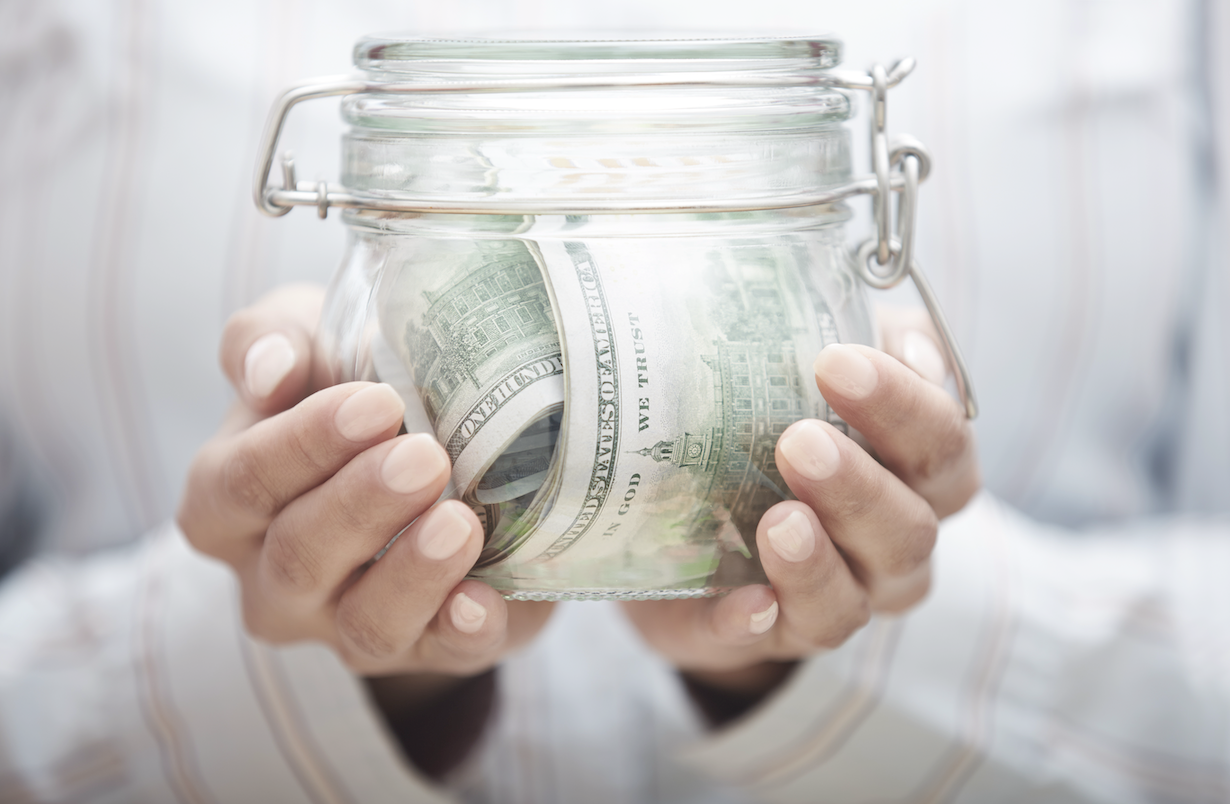 A person is holding a jar filled with money.