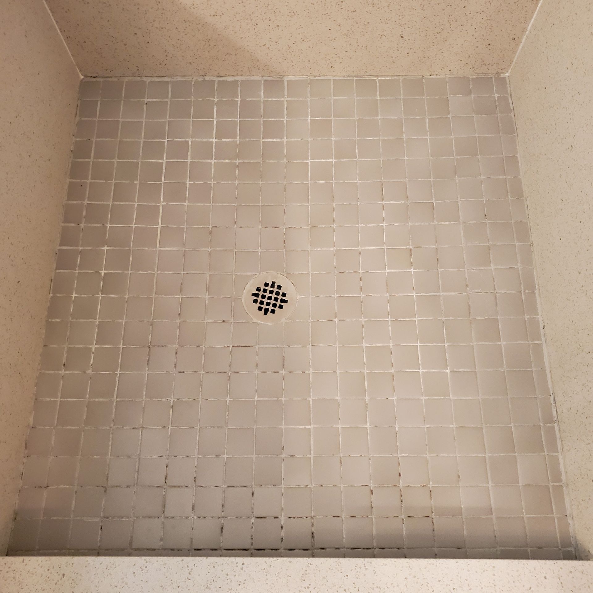 A shower stall with white tiles and a drain.