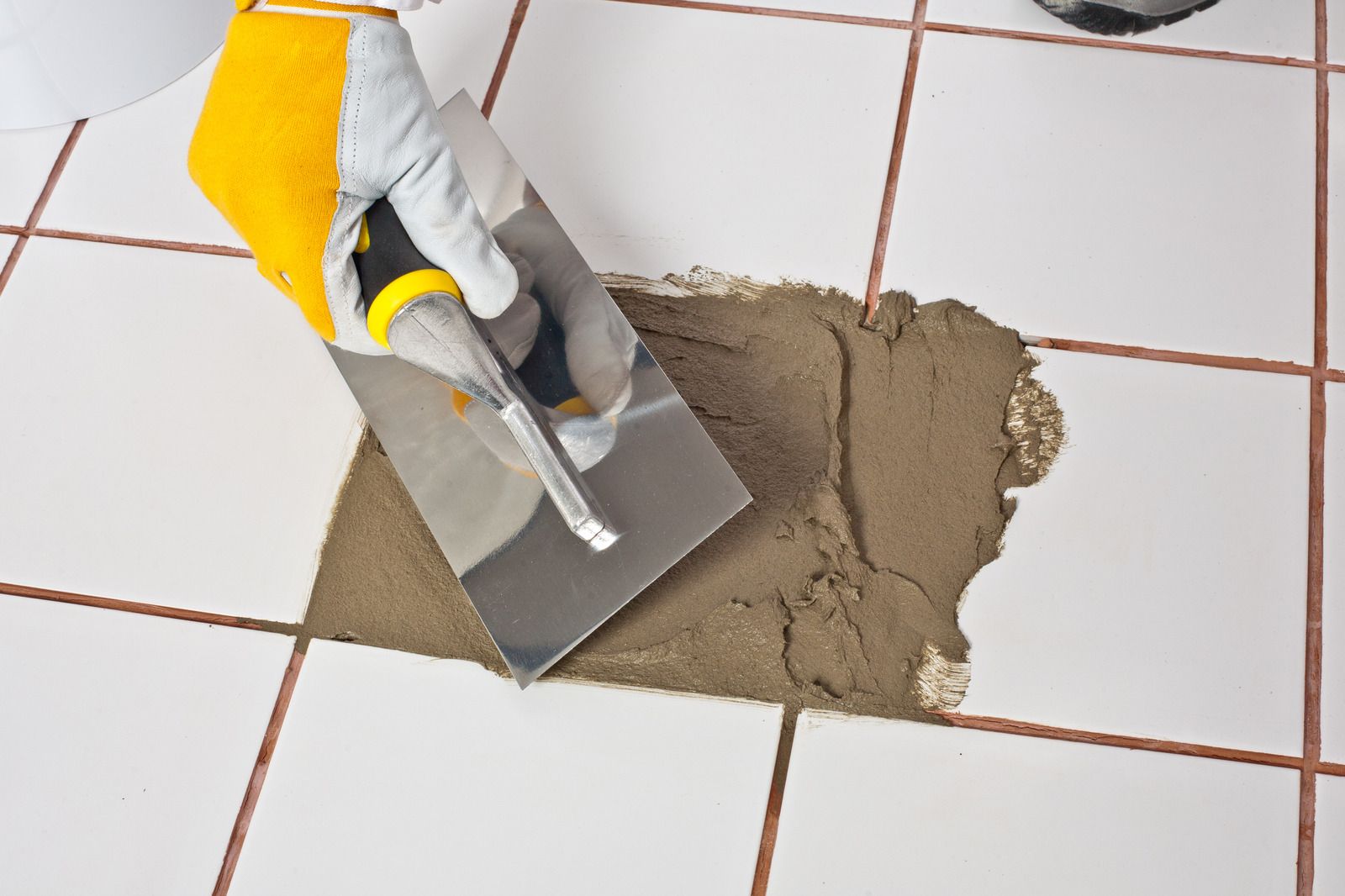 Person using a trowel to apply grout to white tiled floor.
