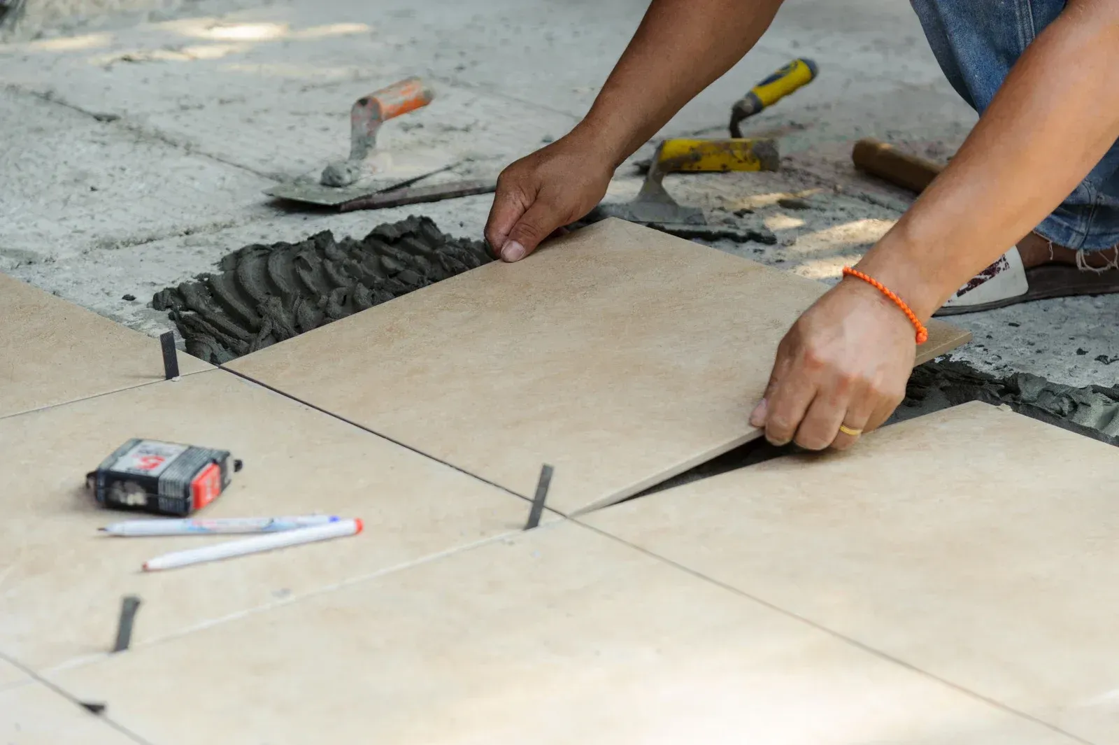 A man is laying tiles on a concrete floor.