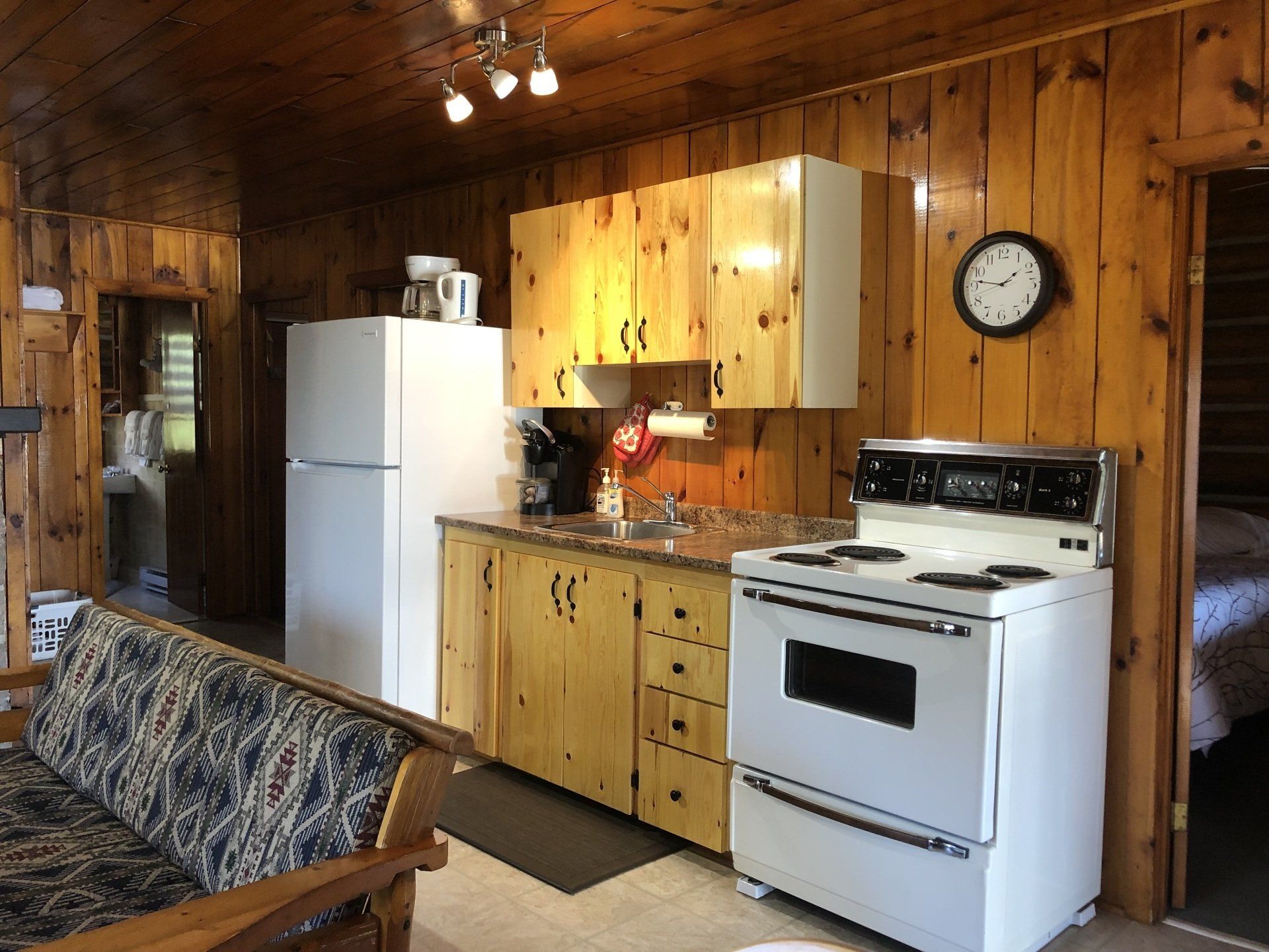 White Pine cottage kitchen with a stove, refrigerator, sink and a clock on the wall.