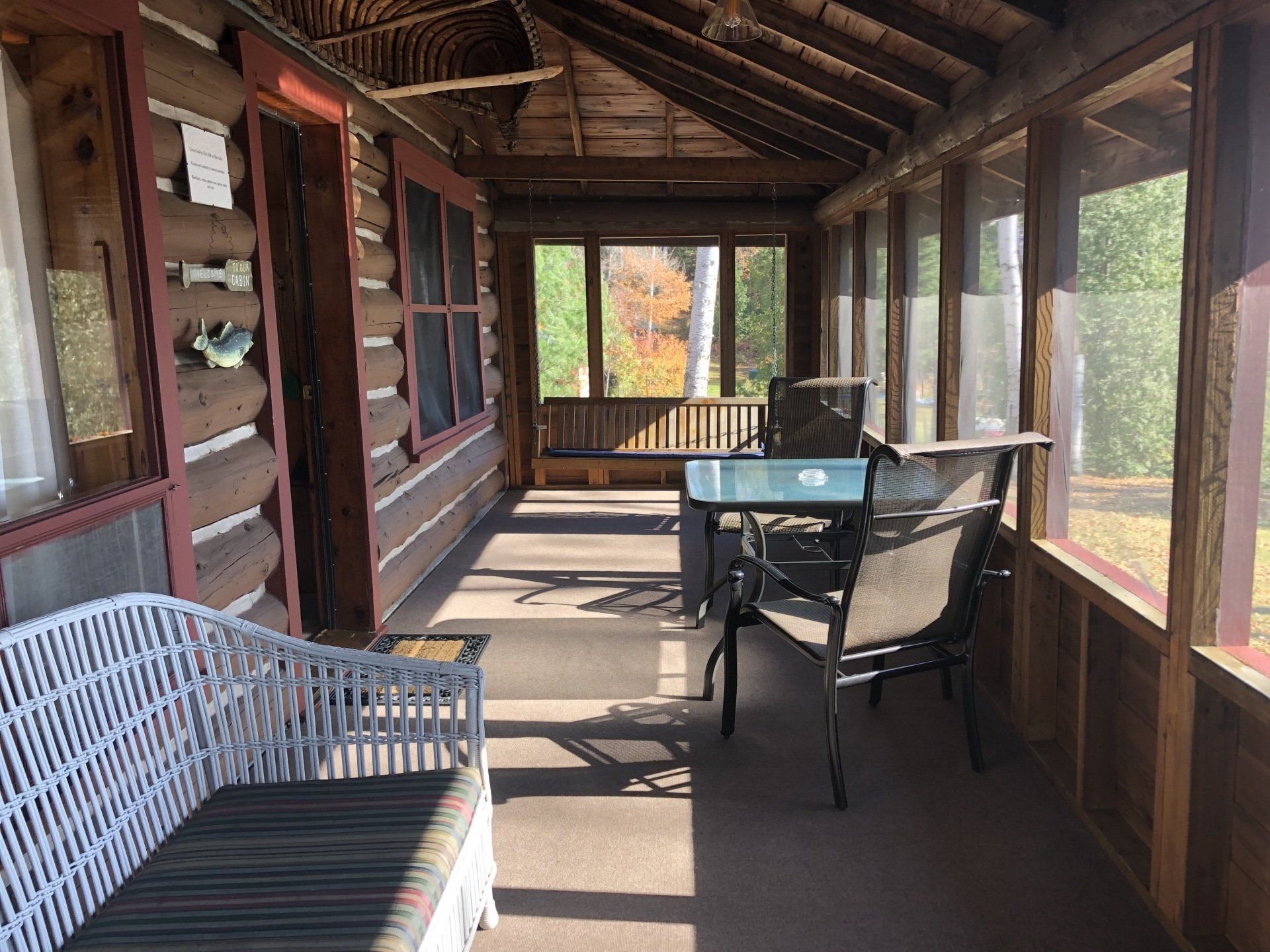 A screened in porch with a wicker couch , table and chairs.