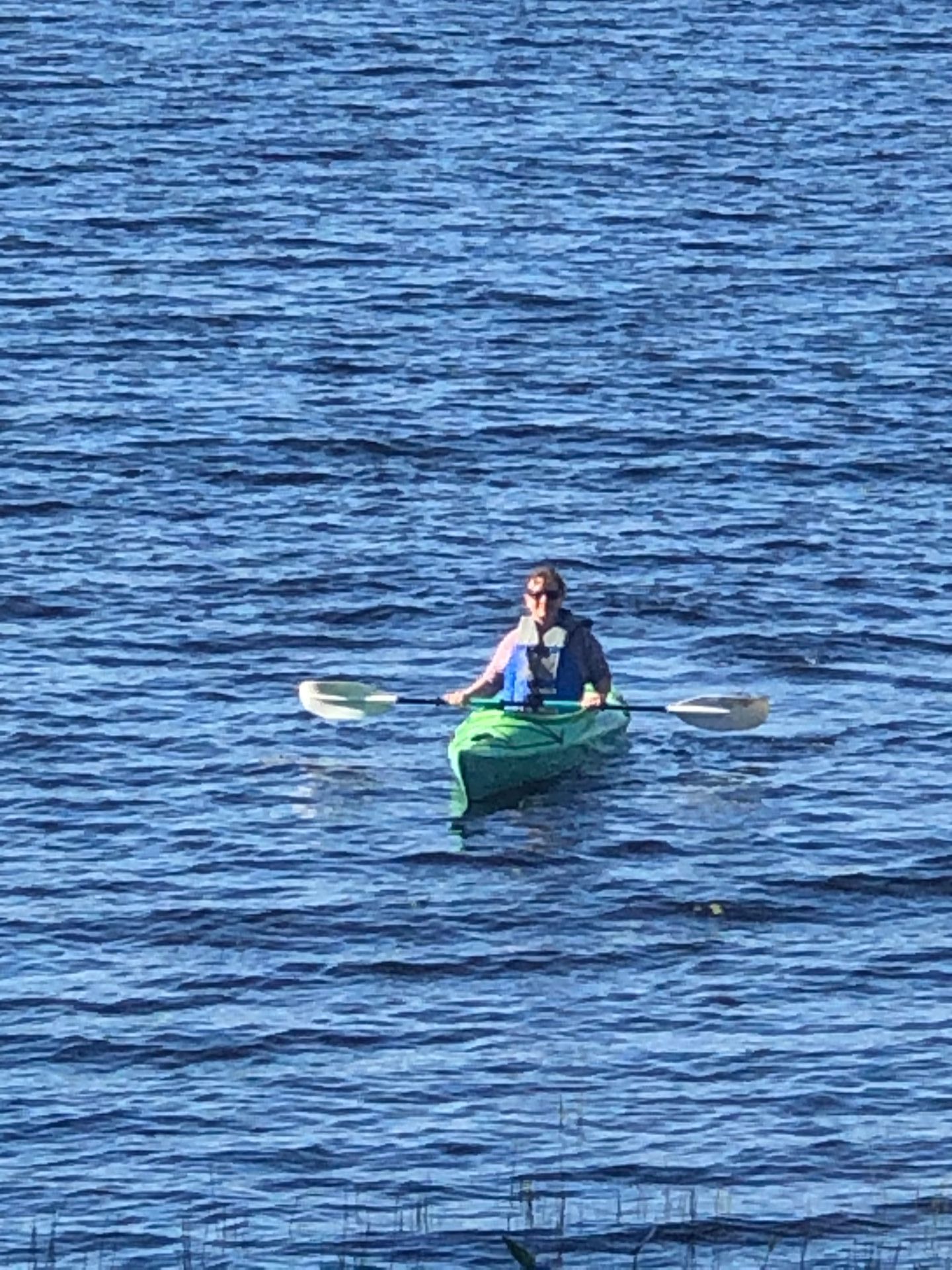 A man is paddling a green kayak on a lake.