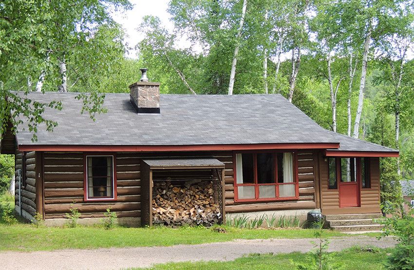 White Pine cottage with a stack of logs in front of it