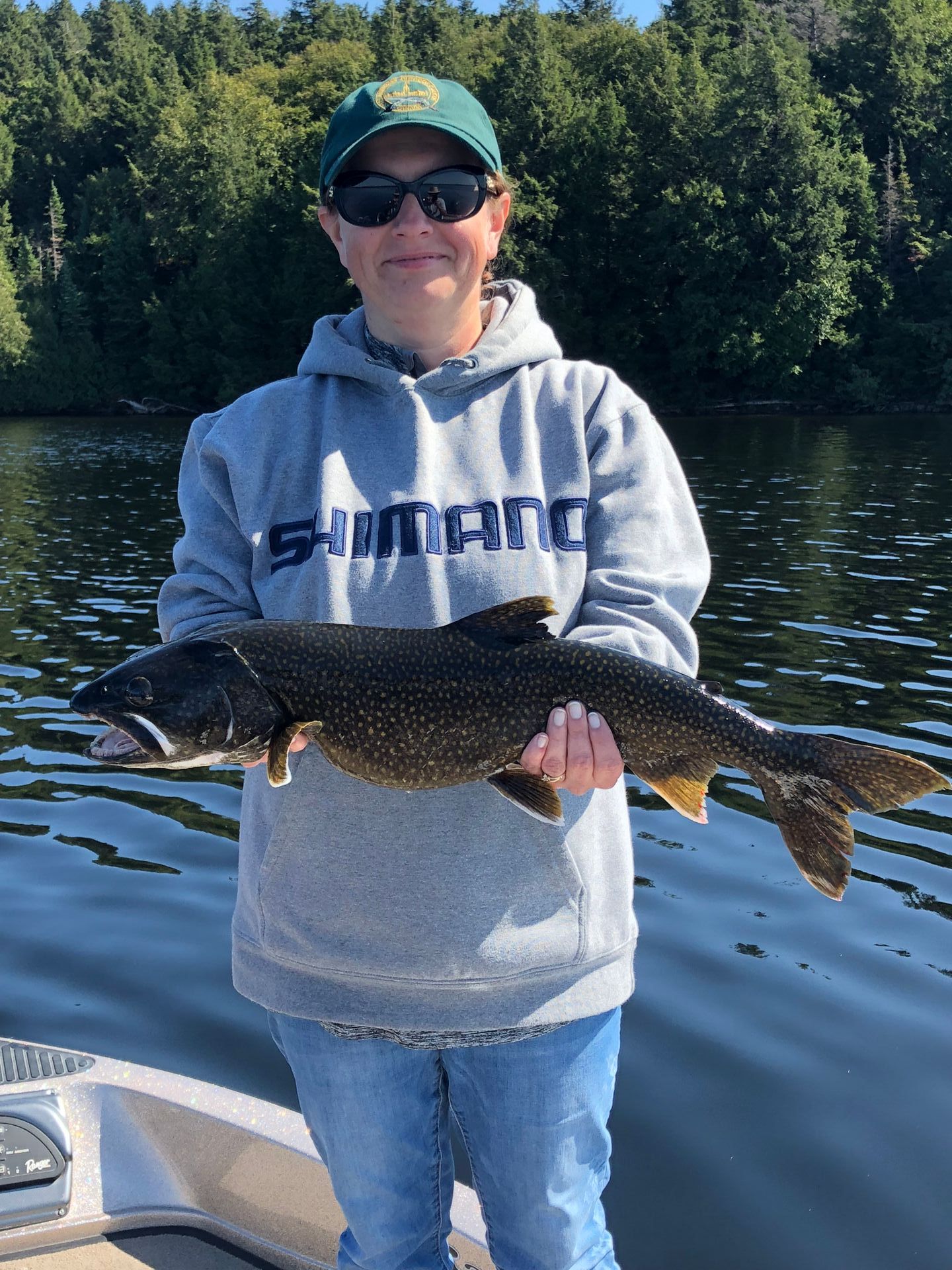 A woman is holding a large fish in front of a lake.
