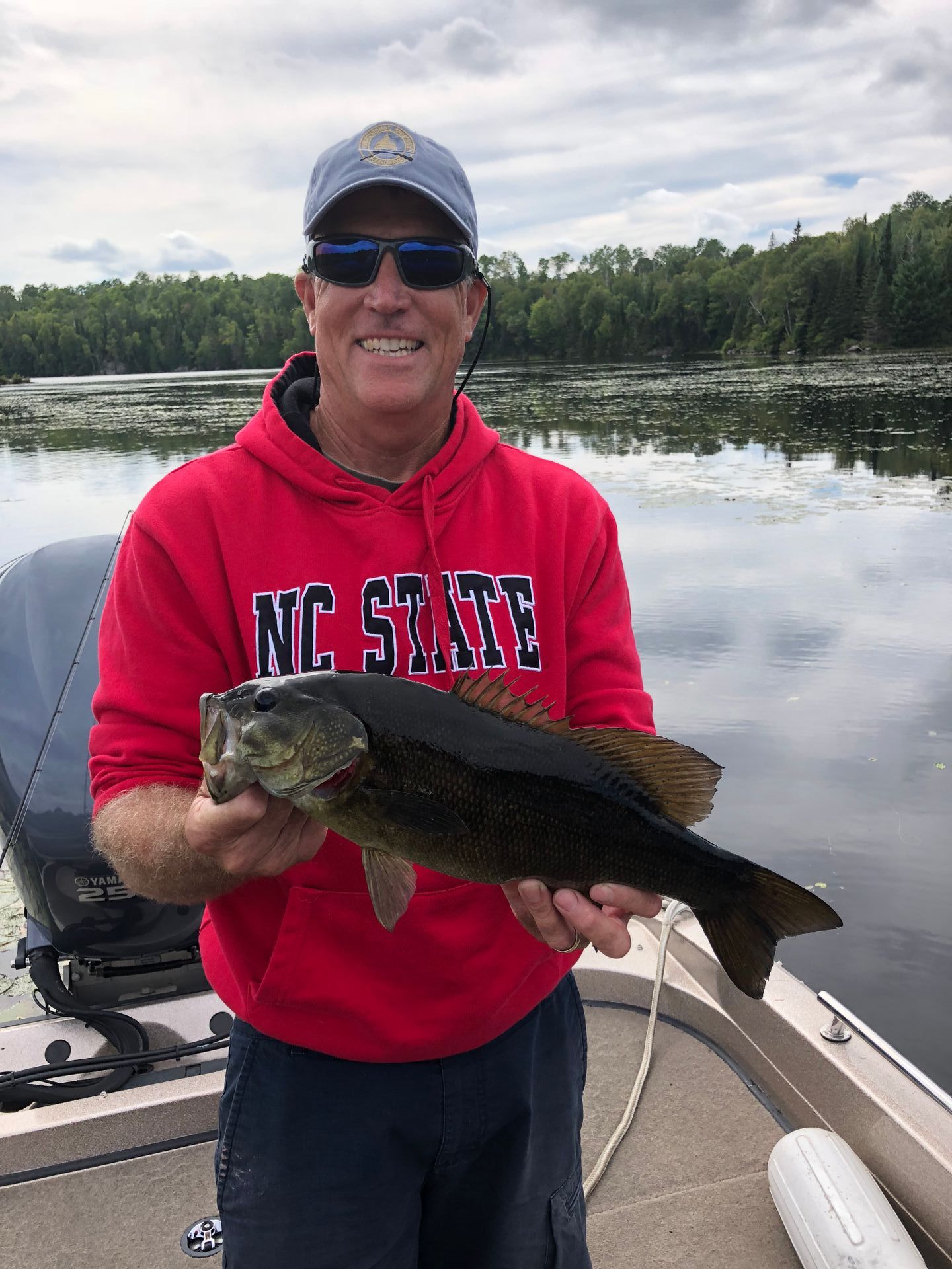 A man in a red nc state hoodie is holding a large fish on a boat.
