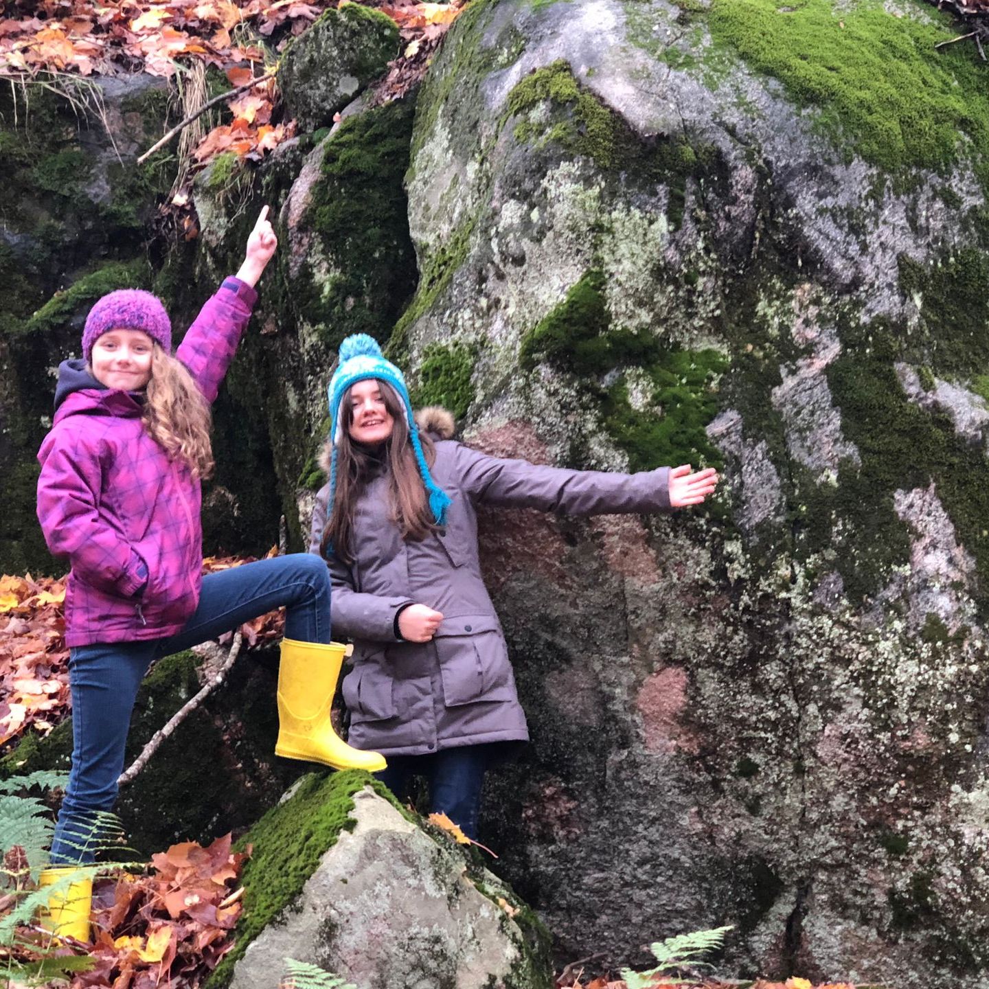 Two girls are standing next to each other on a rock in the woods.