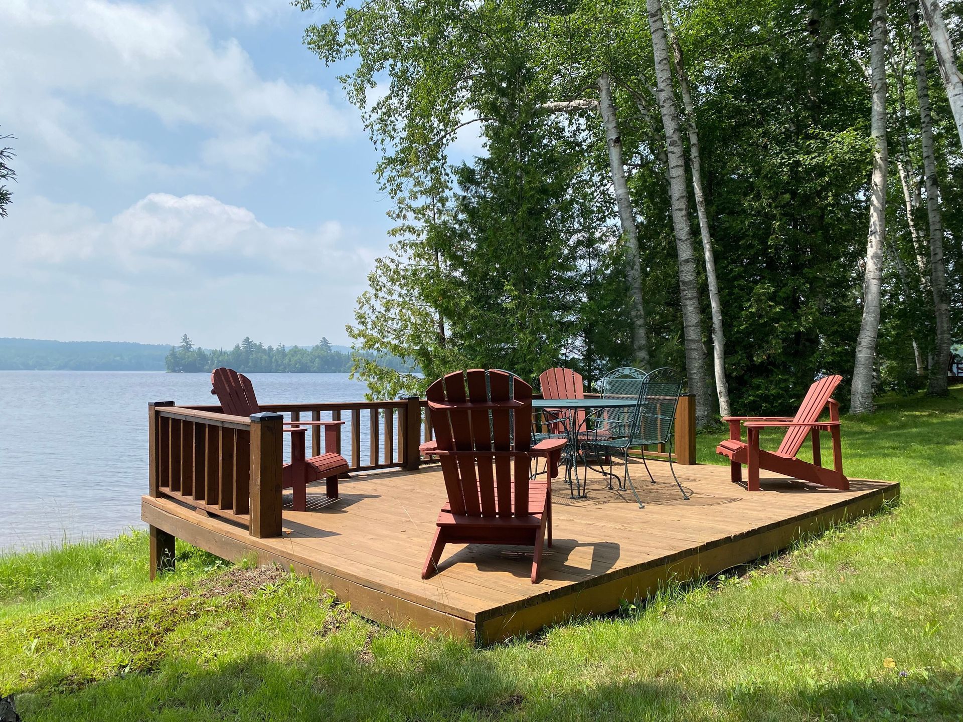 A wooden deck with chairs and a table overlooking a lake.