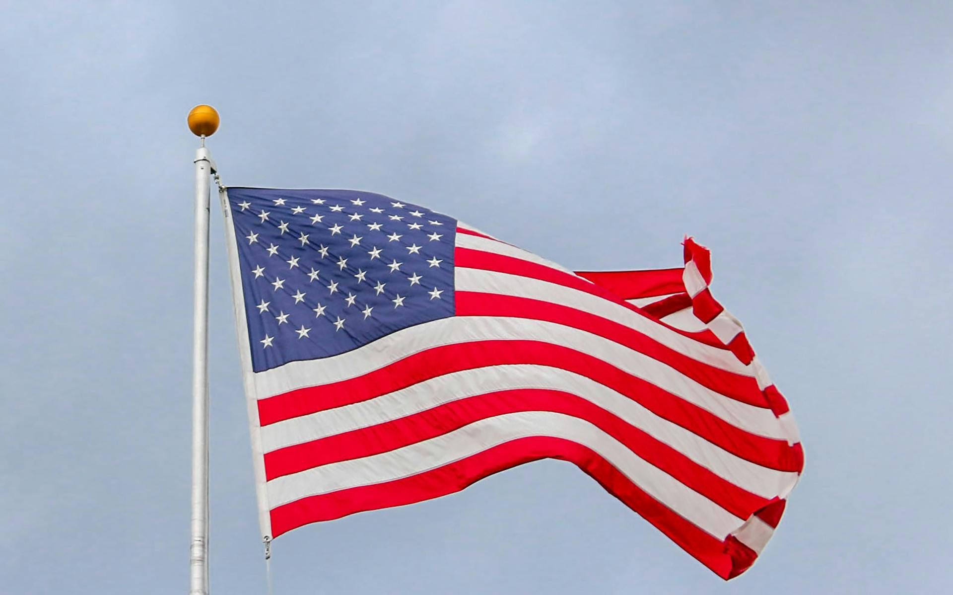 American flag waving on a pole against a cloudy sky.