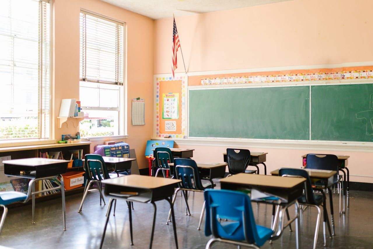 Empty classroom with desks, a chalkboard, and American flag.
