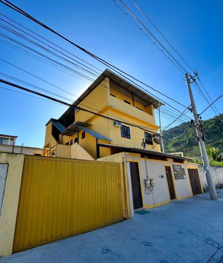 Um prédio amarelo de três andares com um portão de metal e uma escada externa, visto de uma rua sob um céu azul claro.