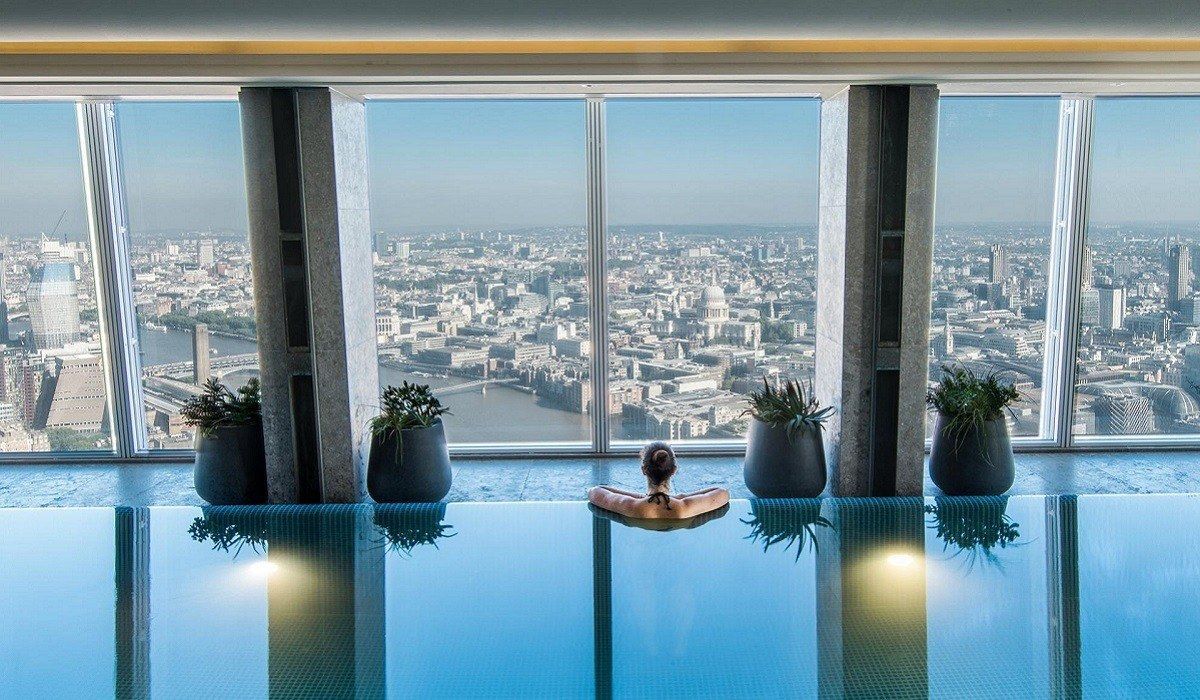 Uma pessoa relaxa em uma piscina infinita coberta, com vista panorâmica para o horizonte da cidade, a partir de um arranha-céu.