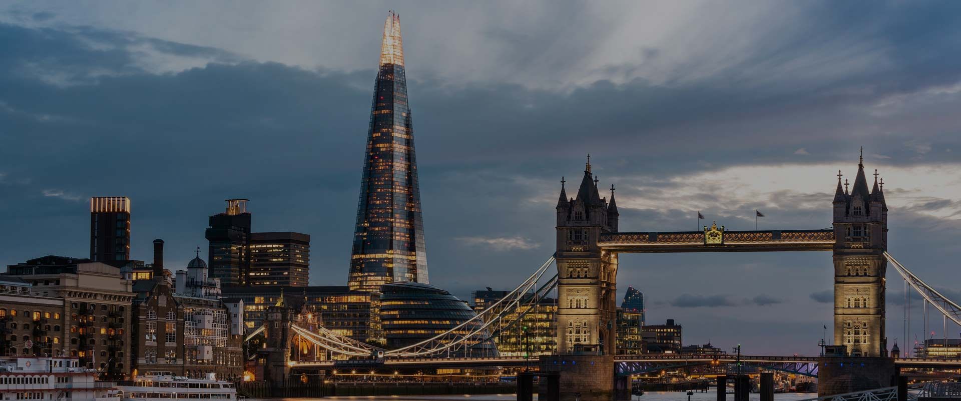 O arranha-céu The Shard se ergue acima do horizonte de Londres ao lado da iluminada Tower Bridge ao entardecer.