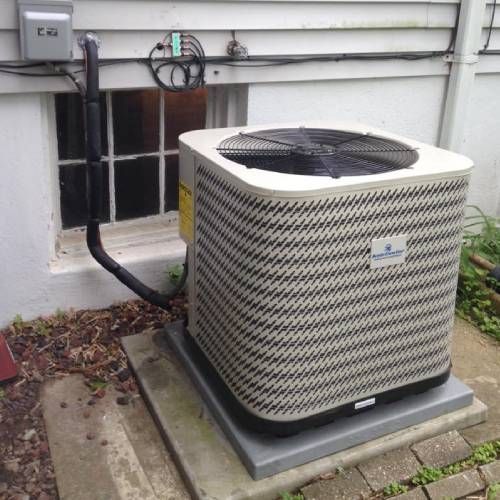 An air conditioner is sitting outside of a house next to a window.