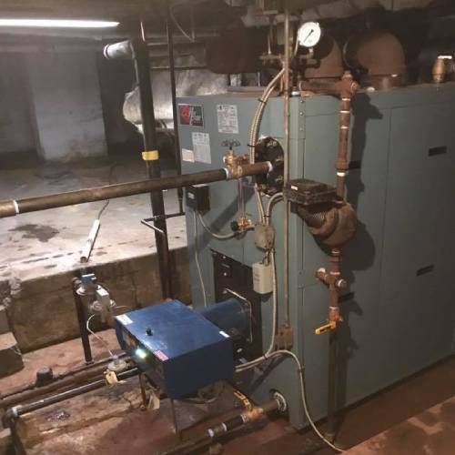 A blue boiler is sitting in a basement next to pipes.