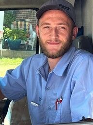 Man with beard in blue shirt and cap smiles in a vehicle.