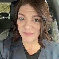 Woman with brown hair in car, looking at the camera. Wearing a dark blue jacket.