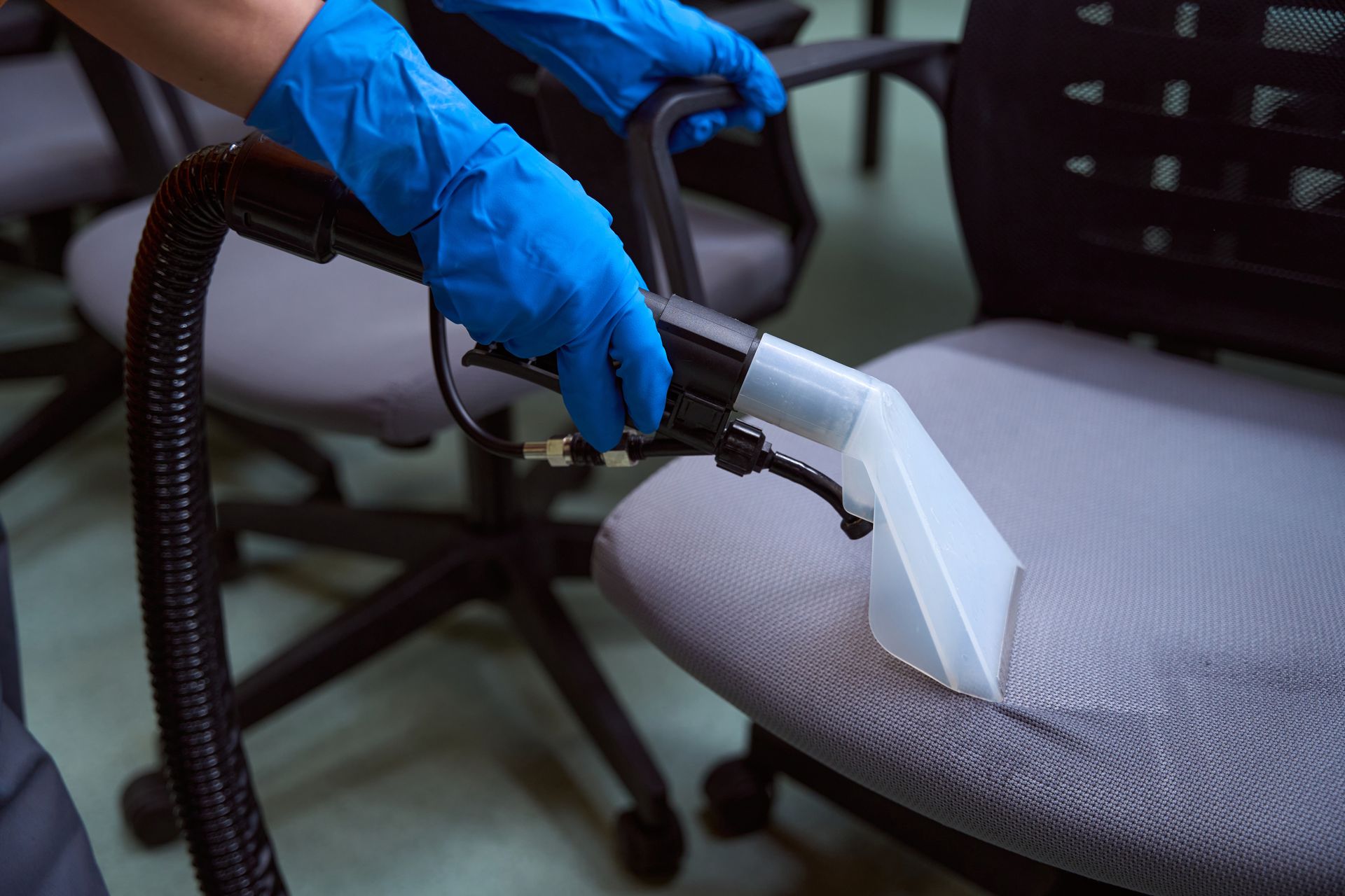 A person is cleaning an office chair with a vacuum cleaner.