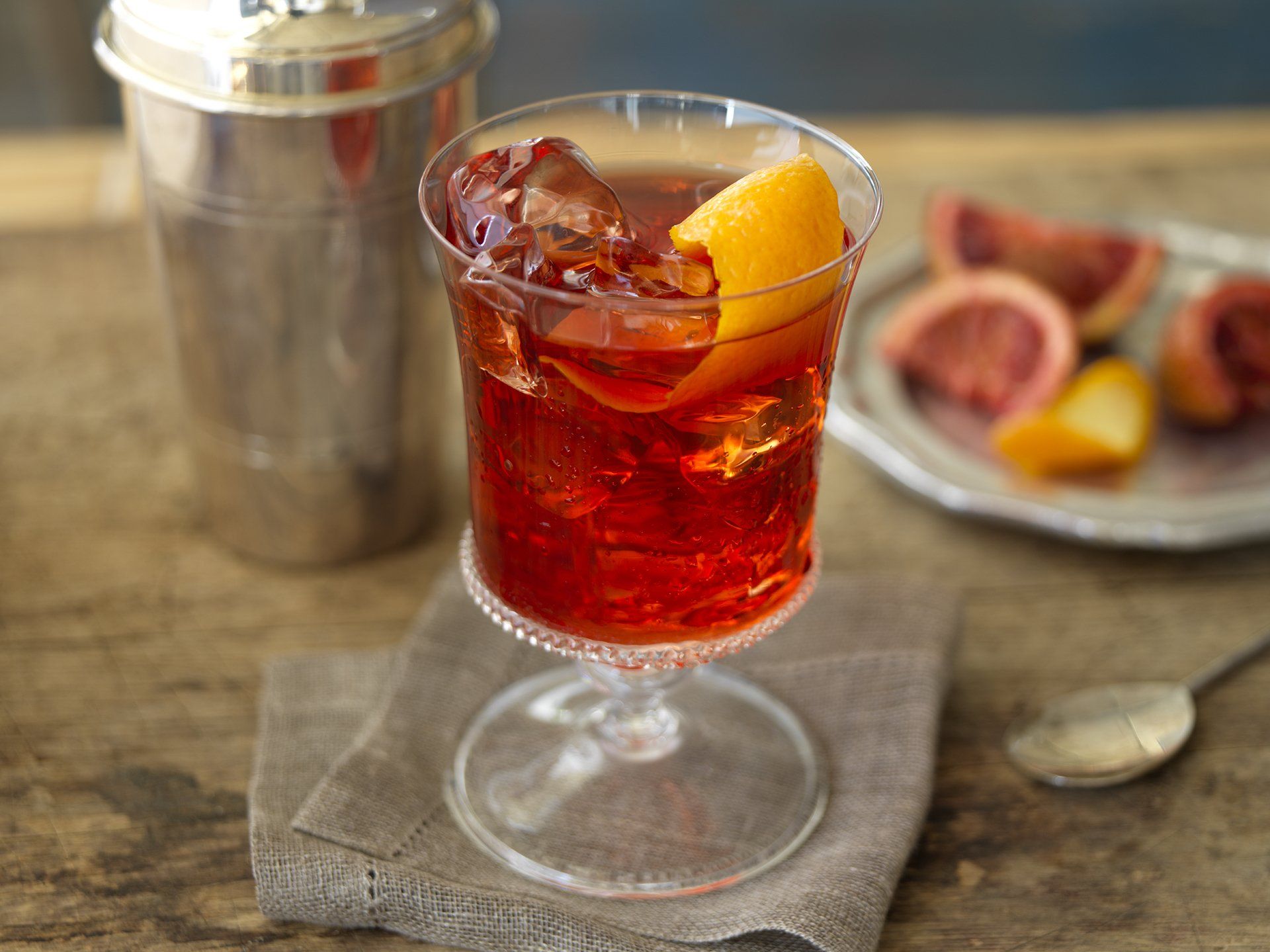 A glass of red liquid with ice and an orange slice on a table.