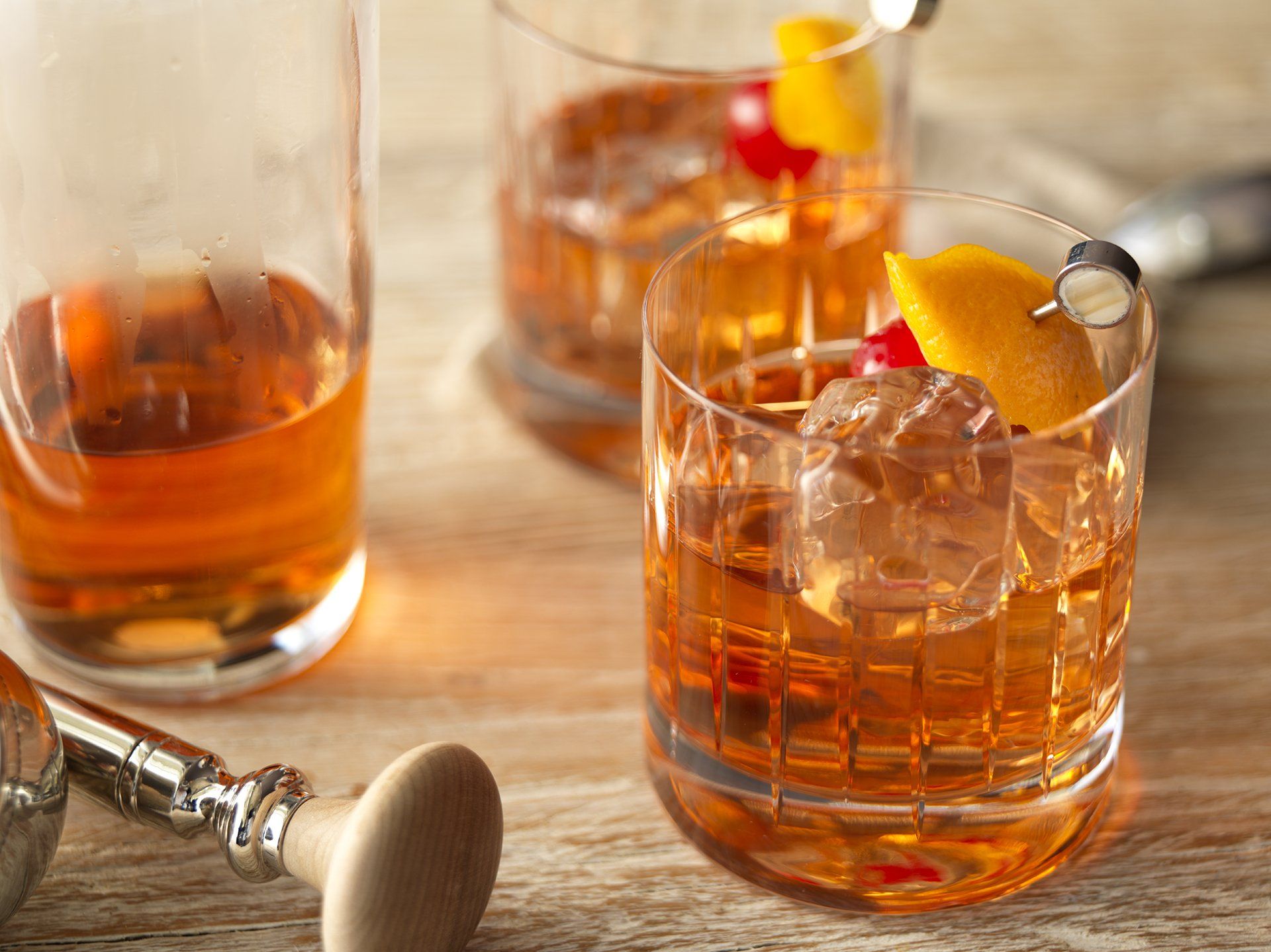 Three glasses of whiskey are sitting on a wooden table.