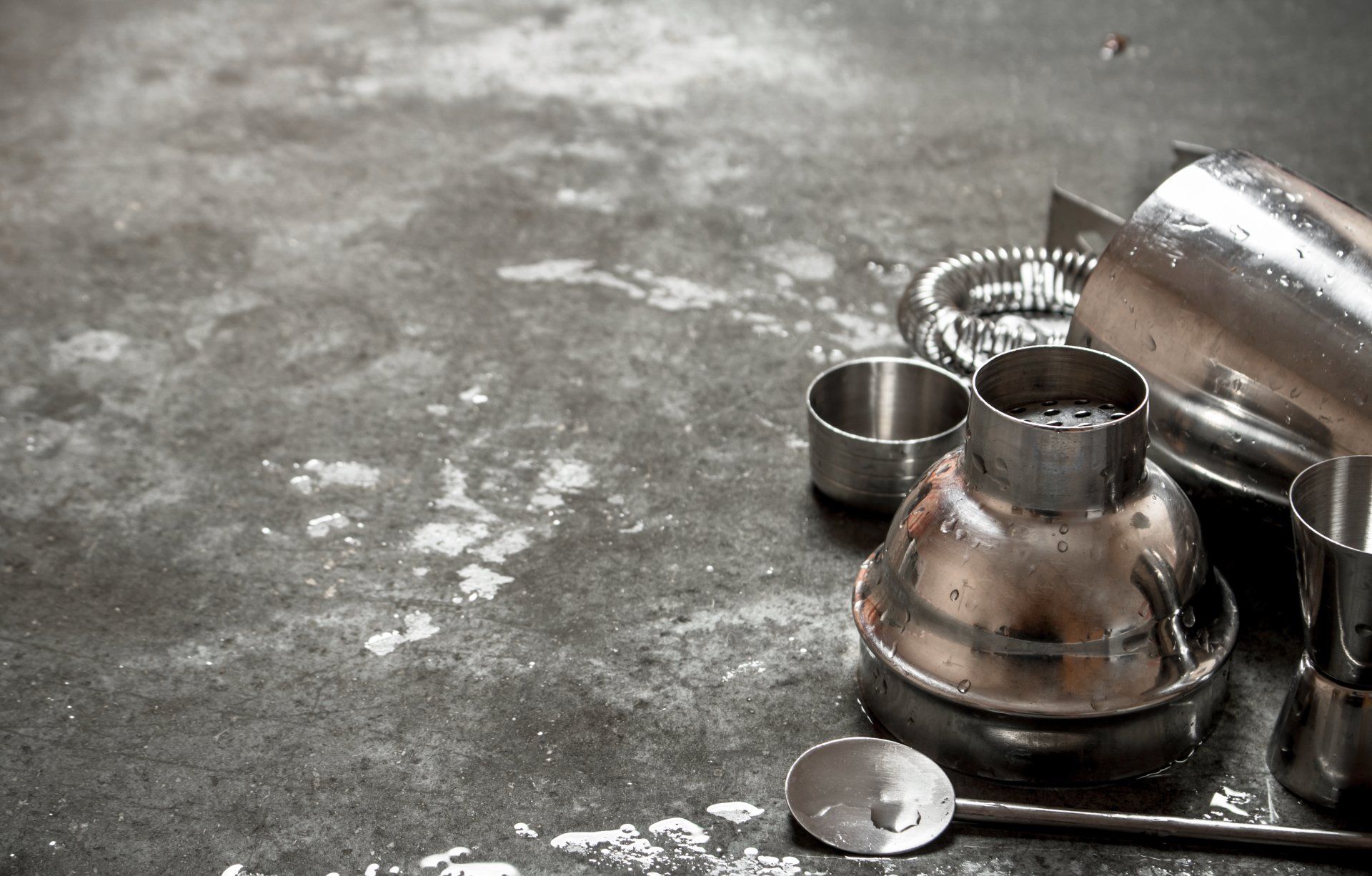 A black and white photo of a shaker , measuring cups , and a spoon on a table.