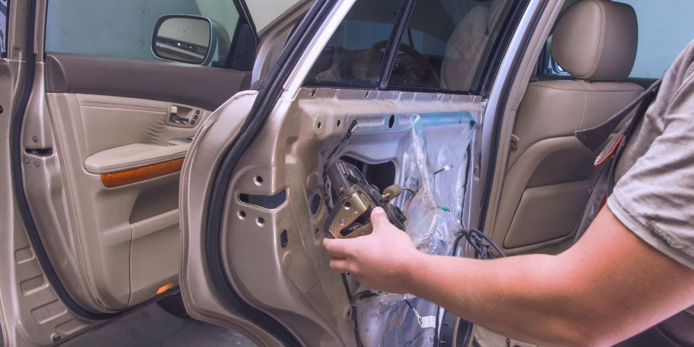 Locksmith attempting to unlock a car door using a lockpicker tool.