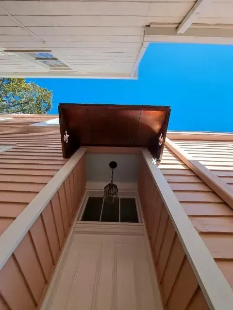 Low-angle shot of a door under a copper-colored awning. Light pink siding with white trim. Blue sky visible.