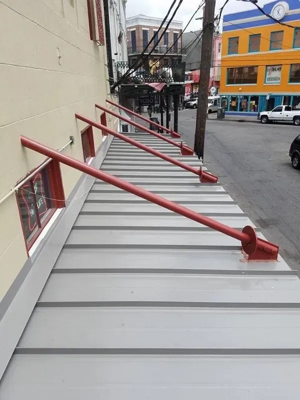 Red metal supports brace a gray metal awning attached to a beige building. Street scene in background.