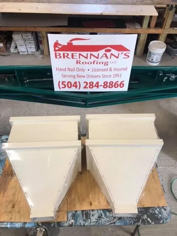 Four cream-colored metal roofing boxes on wood, with a Brennan's Roofing sign behind them.