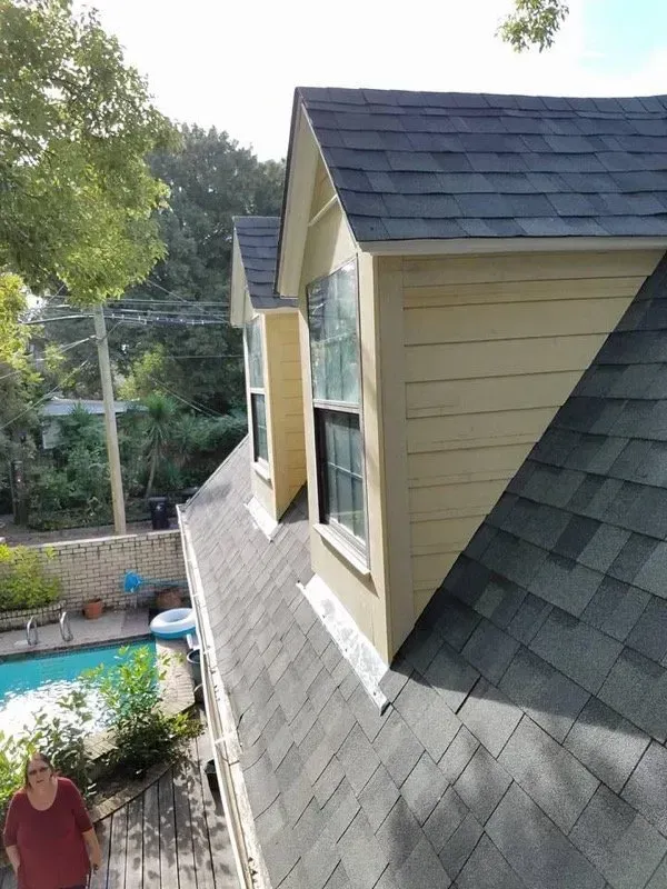 A roof with two dormer windows, pool in the background, person standing below.