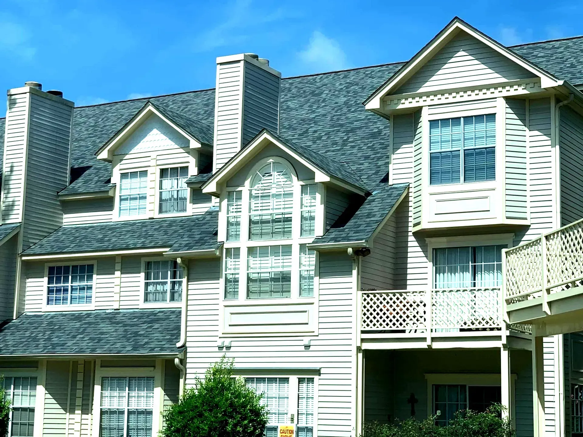 Multi-story townhouses with gray shingle roofs, beige siding, and multiple windows against a blue sky.