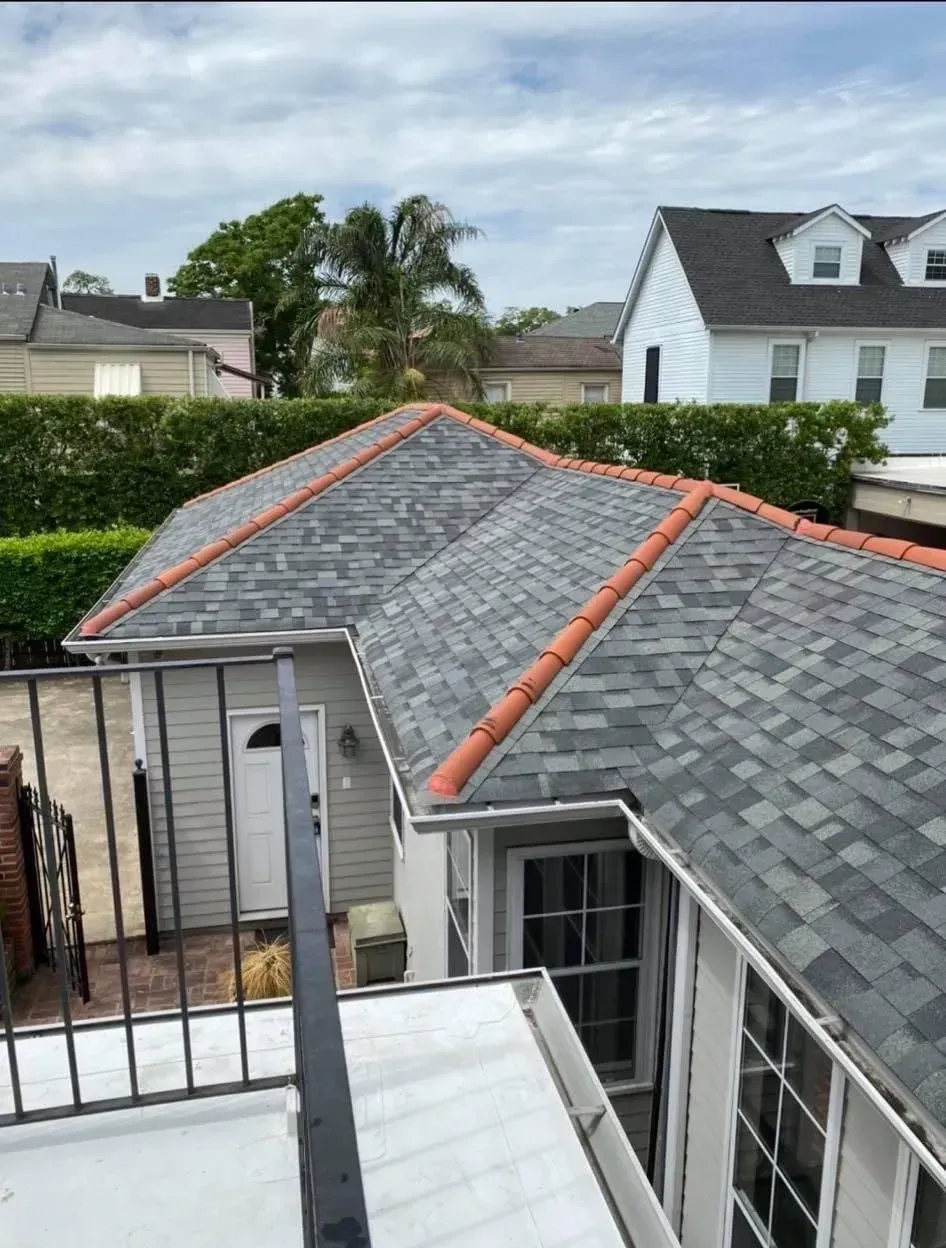 Gray shingled roof with orange trim, viewed from above a balcony, with a clear sky backdrop.