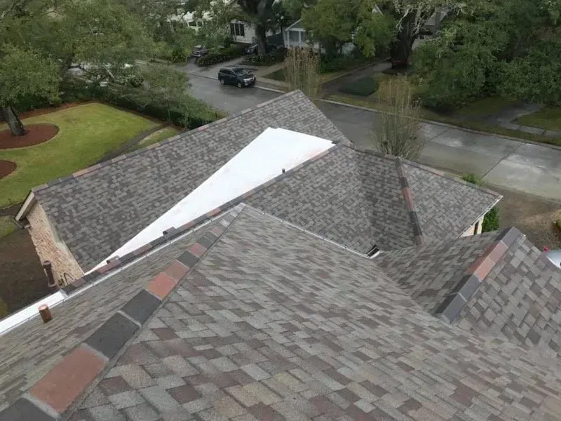 Overhead view of a home with a multi-colored shingle roof, green lawn, and street with a car.