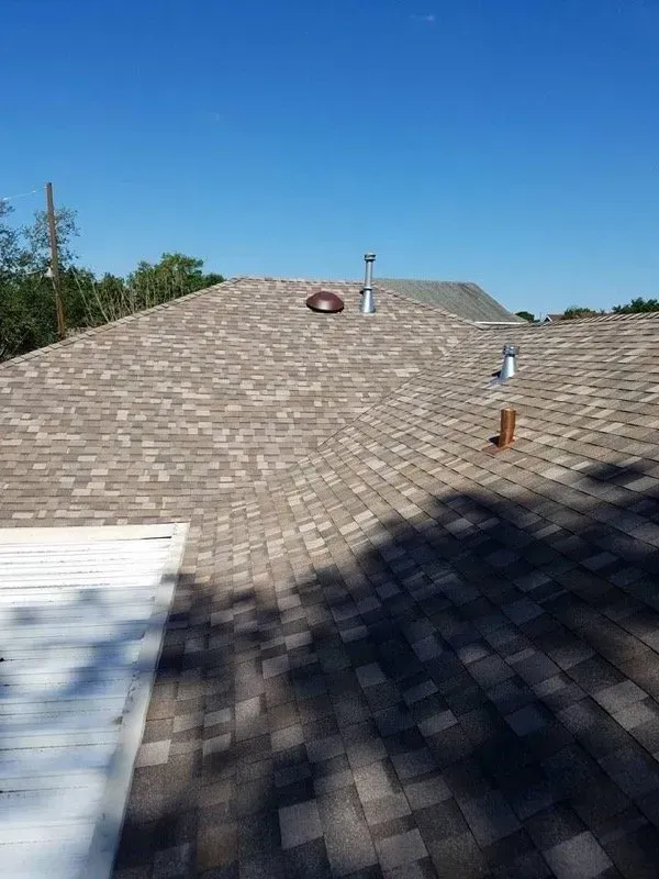 A roof covered in brown and gray shingles with a blue sky background.