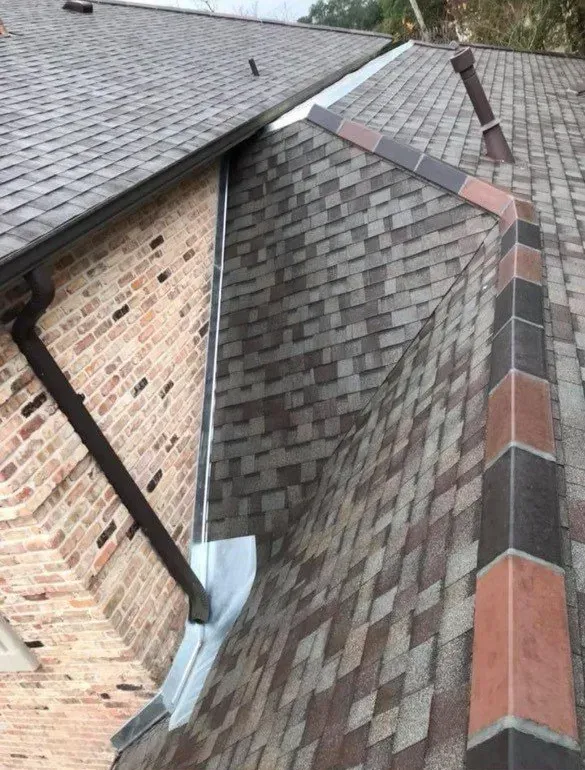 Brown shingle roof with a dark gutter and brick wall. Some discoloration visible on the shingles.