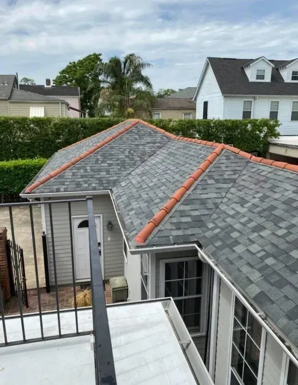 View of a gray shingled roof with orange trim, viewed from above, with buildings and a cloudy sky in the background.