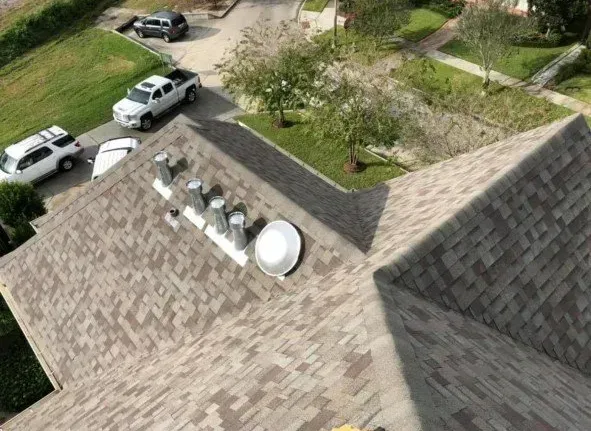 Overhead view of a roof with ventilation systems, cars parked on the street, and surrounding greenery.