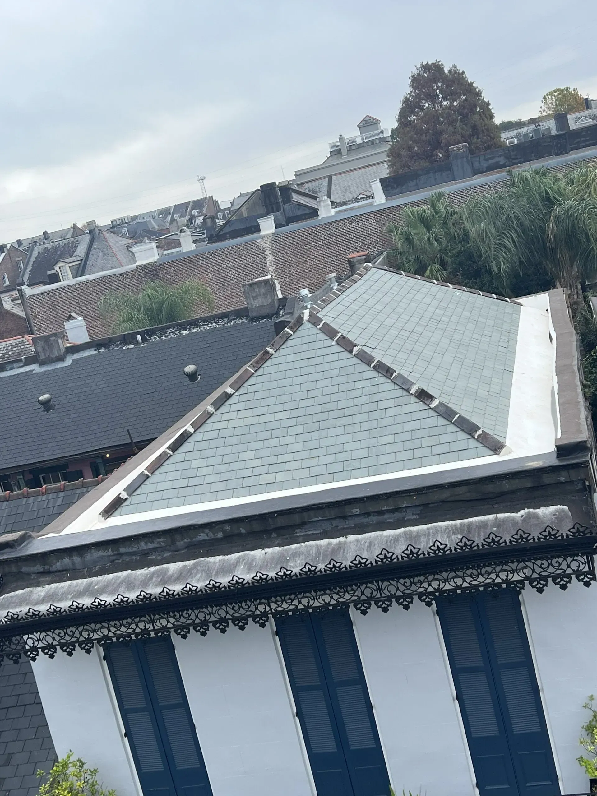 A building with a slate roof and ornate trim, viewed from above, with other buildings in the background.
