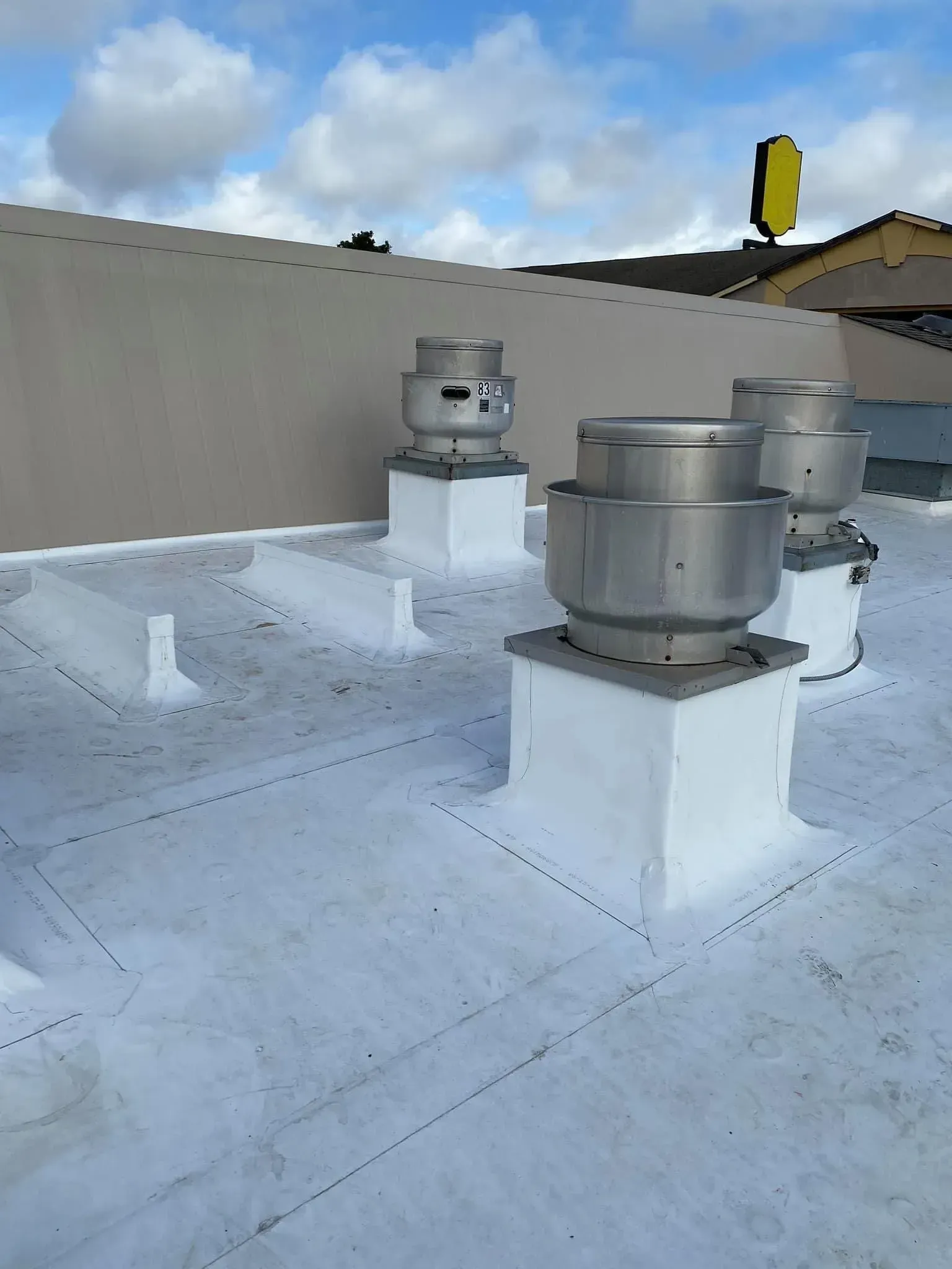 White roof with three stainless steel vents, against a cloudy sky.