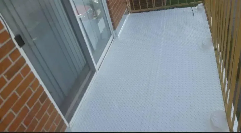 Small balcony with white surface, beside a brick wall and wooden railing.