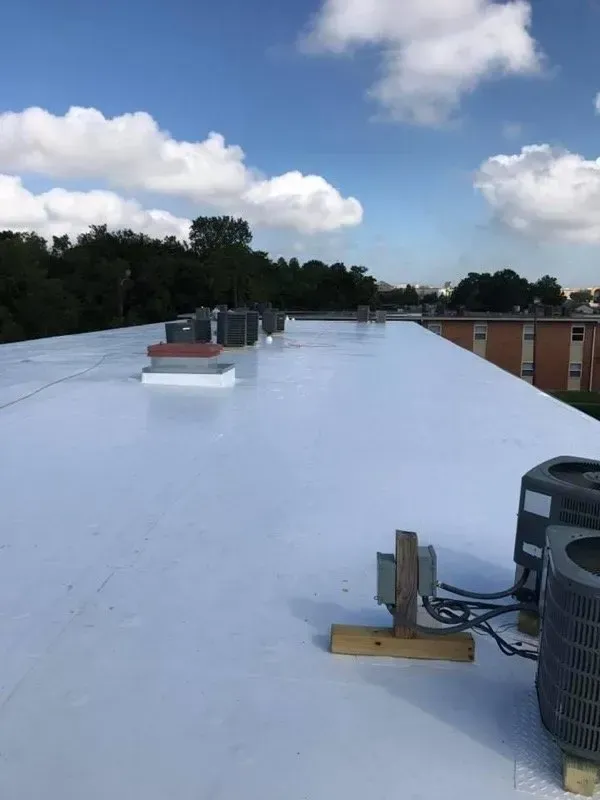 White flat roof with HVAC units under a blue sky with clouds.