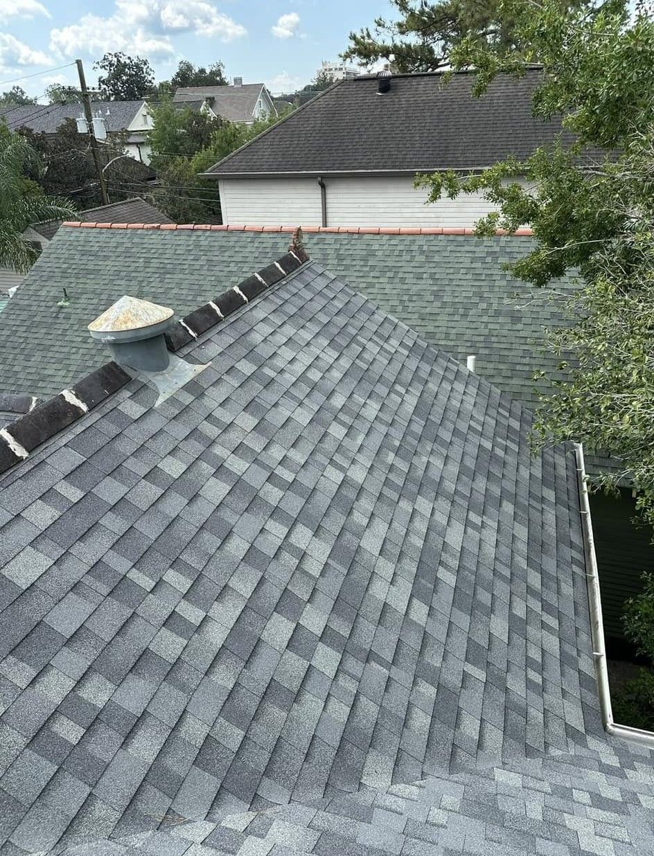 Gray shingle roof of a house with a chimney and part of a green roof visible.