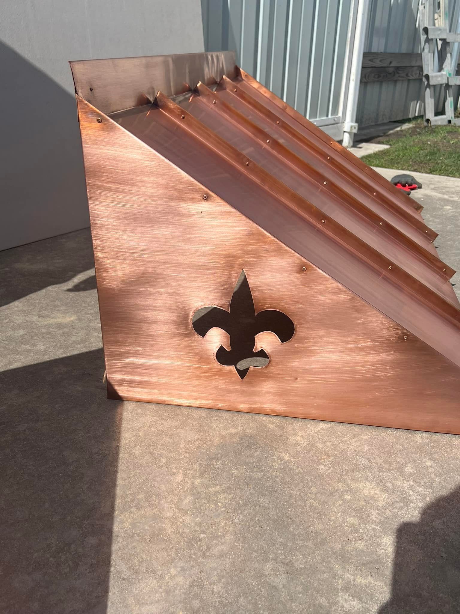Copper roof flashing with Fleur-de-lis cutout, resting outdoors.