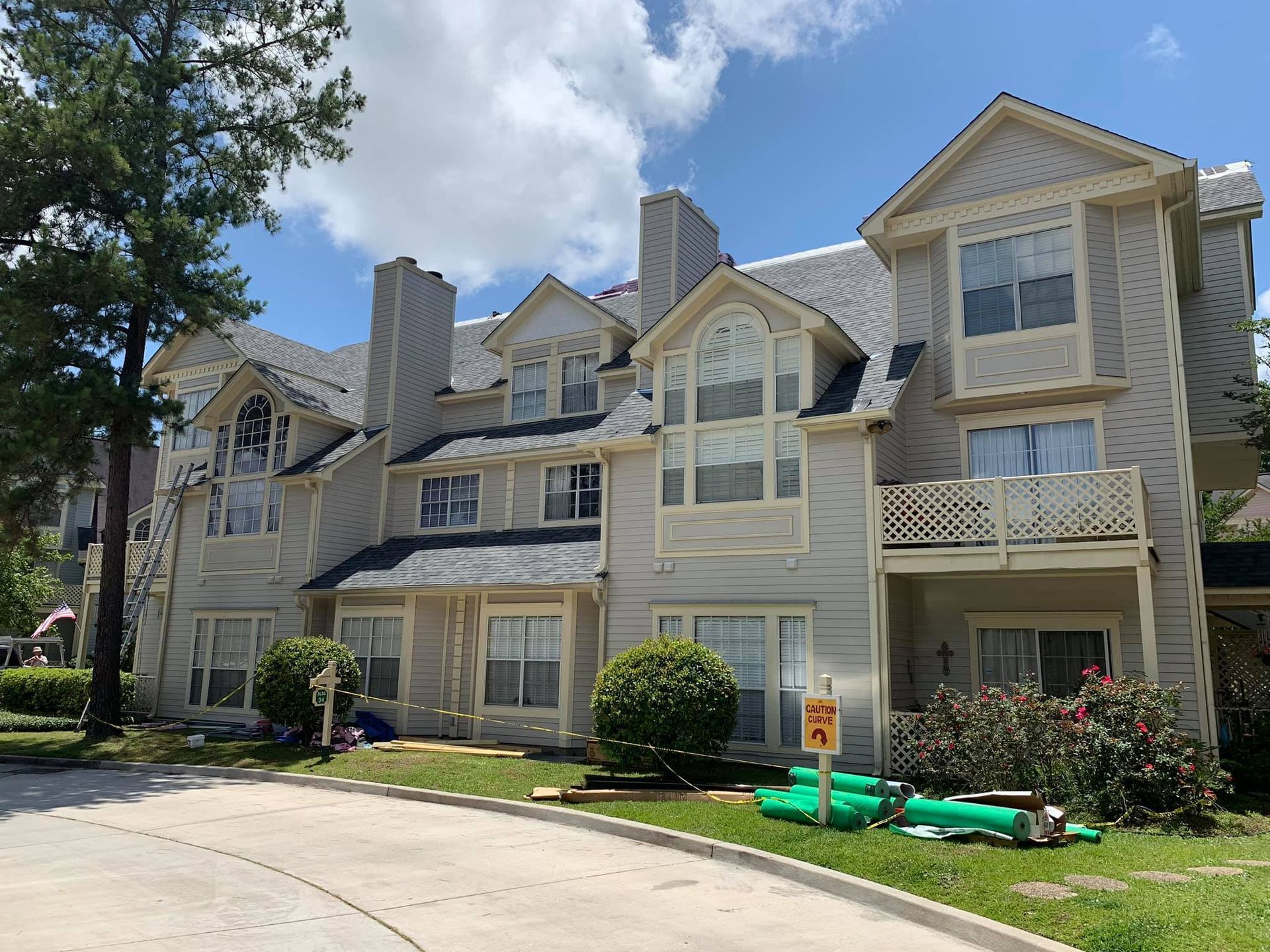 Beige apartment building with dark roof, windows, and greenery. Sunny day.