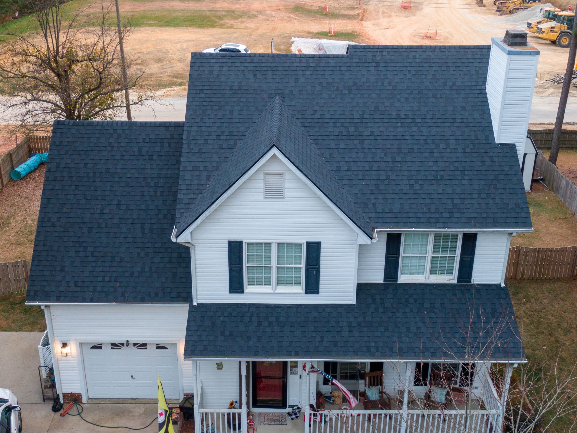 Rooftop deck with white surface, black railing, and grey siding. Buildings and trees in the background.