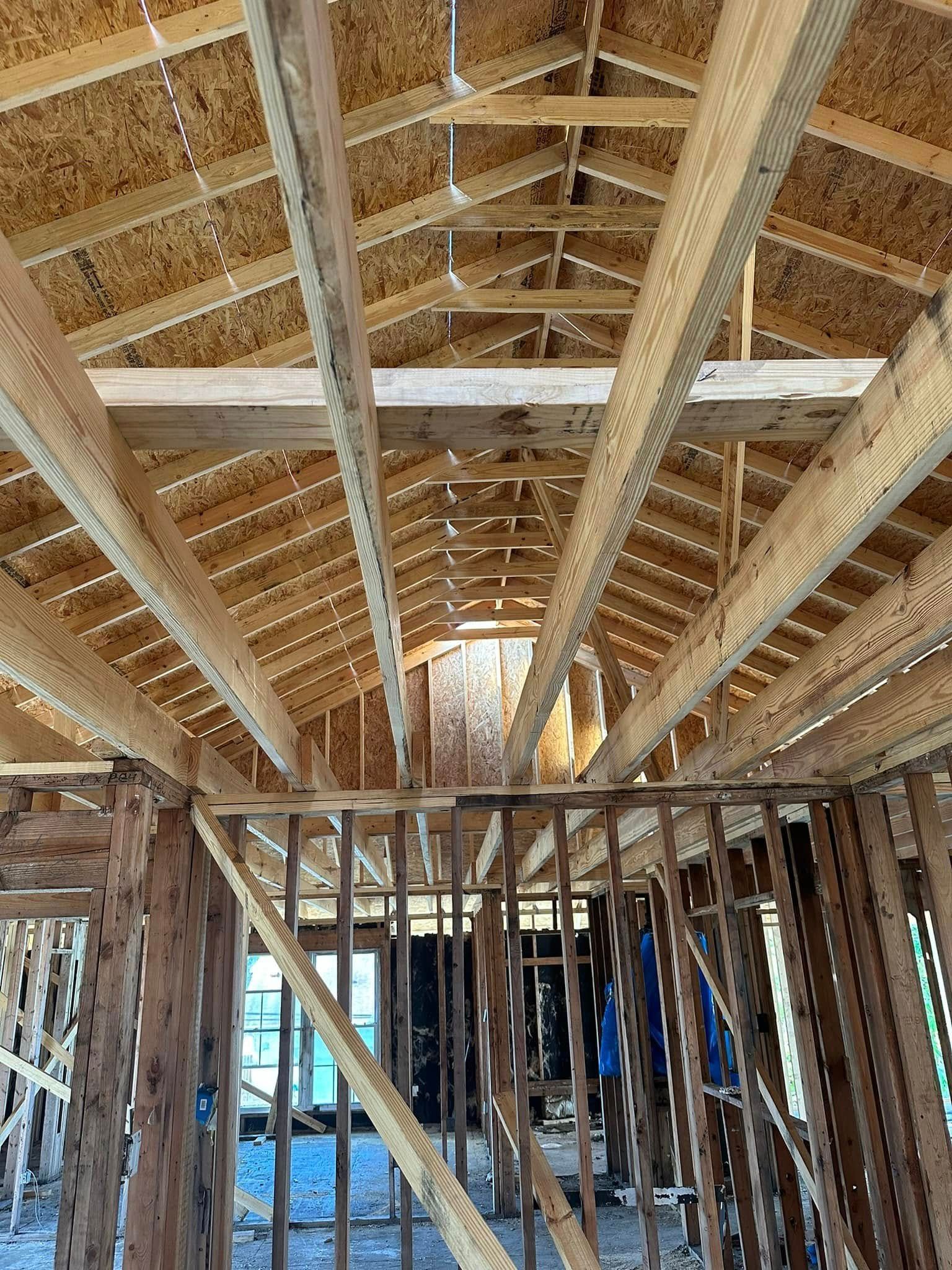 Interior view of a building under construction, showing exposed wooden beams, rafters, and framing.
