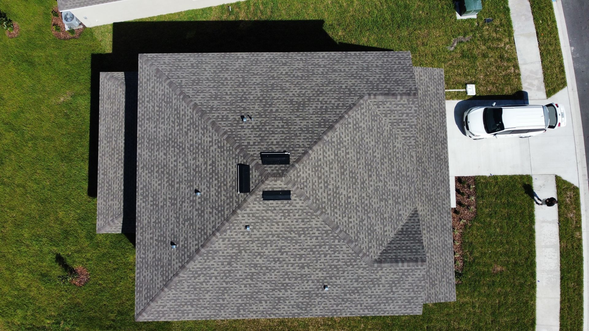 Overhead view of a gray shingled roof with a vehicle parked on a driveway next to a green lawn.