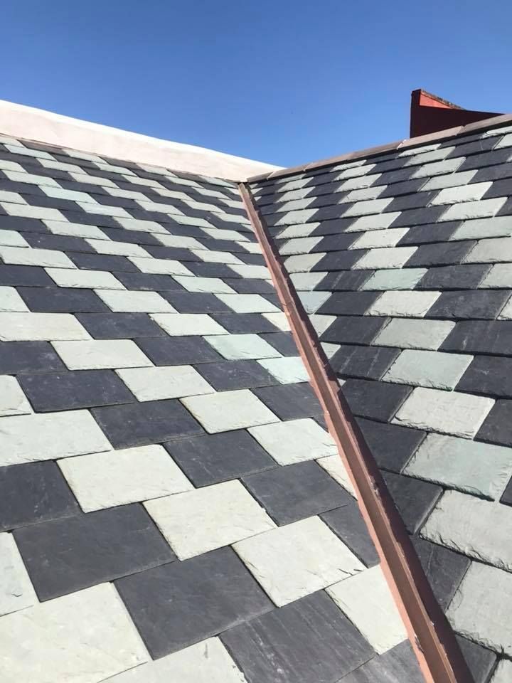 A slate roof with alternating dark and light tiles meeting at a copper-colored valley flashing.